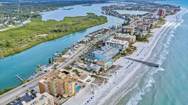 Ein Luftbild einer Küstenstadt mit einer Marina, Strandhotels und einer Brücke, die das Festland mit einer Insel verbindet.