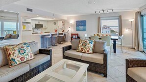 Ein modernes Wohnzimmer mit Korbmöbeln, einem Glastisch und Blick auf die Küche und den Essbereich.