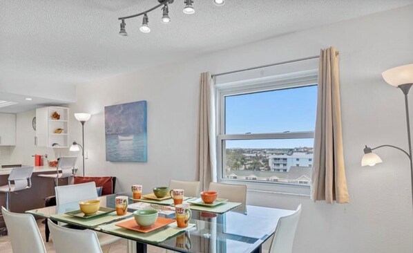 Un comedor moderno con una mesa de vidrio, varias sillas y vista a la ciudad a través de un gran ventanal.