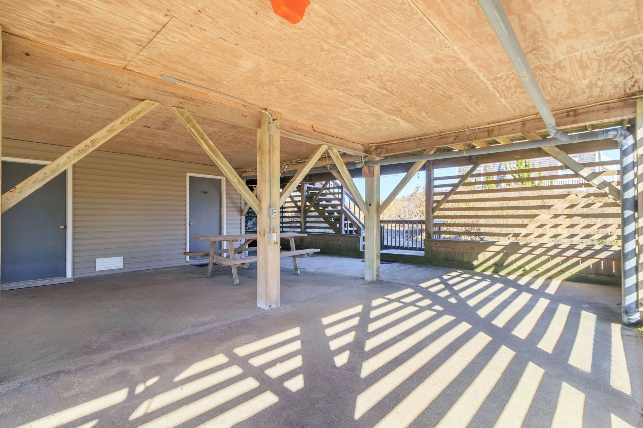 An open-air structure with a wooden roof, concrete floor, and a staircase leading to an upper level.