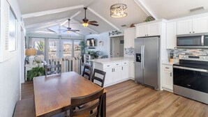 A modern kitchen with white cabinets, stainless steel appliances, and a wooden dining table. - Ocean Views, Gorgeous! Dogs Welcome, Hot Tub, SN9805 (Nags Head)