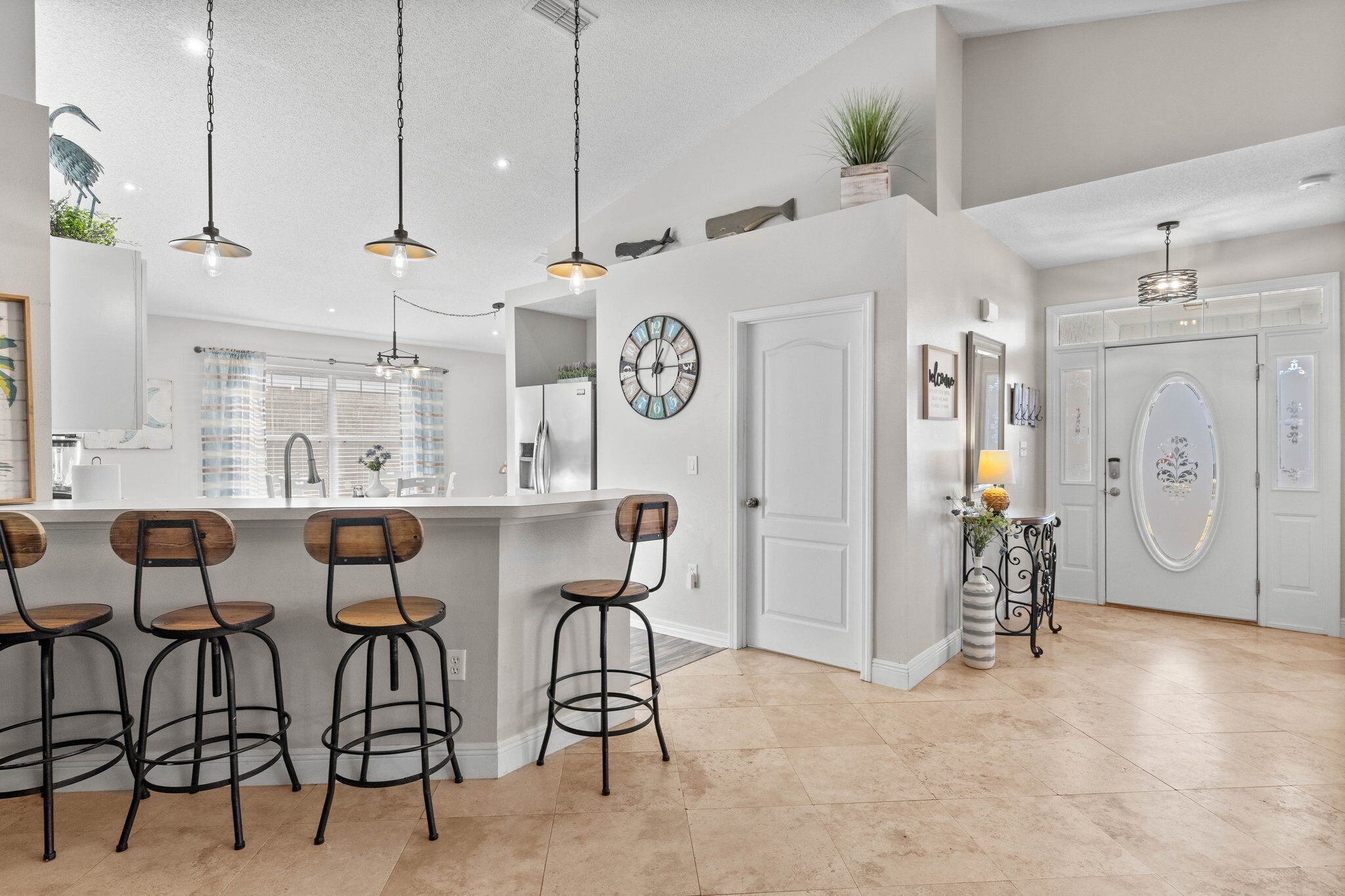 A modern kitchen with a bar area, pendant lighting, and a clock on the wall.