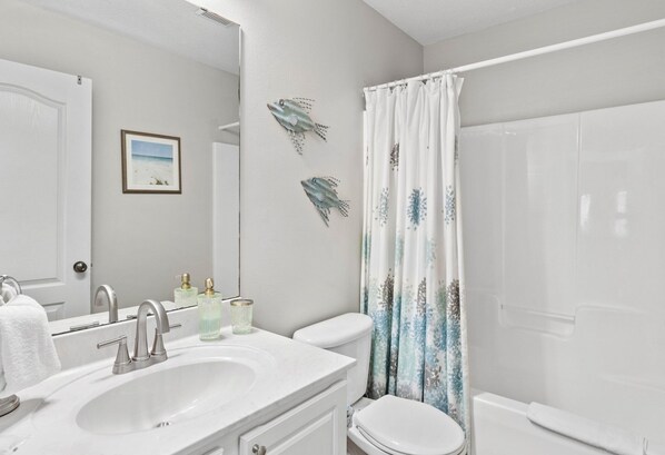 A bathroom with a white sink, a toilet, and a shower. There are decorative fish on the wall and a framed picture above the toilet. - 4BR House with 6-Seat GOLF CART & Hot Tub! Walk to Beach, Covered Patio, Yard (Miramar Beach)