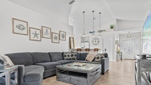 Ein modernes Wohnzimmer mit einem grauen Ecksofa, einem Glastisch mit Stauraum und Wandbildern im maritimen Stil.