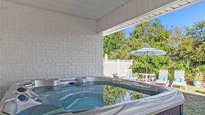 Ein Whirlpool in einer überdachten Außenbereich mit Backsteinmauer, einem Tisch, Stühlen und einem großen Sonnenschirm.
