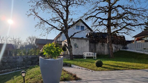 A paved pathway leading to a house with a white exterior, a large planter with a plant, and a bench in the yard. - Holiday Apartment Moises y Ruth with beautiful garden (Murg)