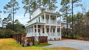 A two-story white house with a balcony, surrounded by trees and a gravel driveway. - Pool, golf cart, nearby attractions & beach + Free Attraction Tickets! (Santa Rosa Beach)