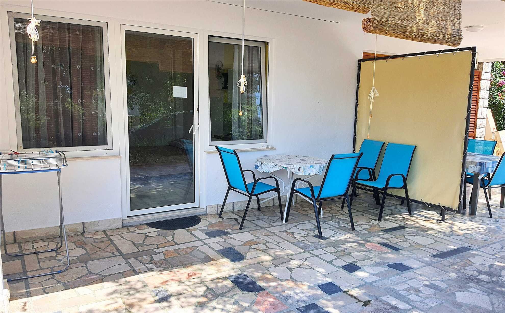 Un patio con una mesa y sillas, un tendedero y un ventanal corredera que da a un jardín.