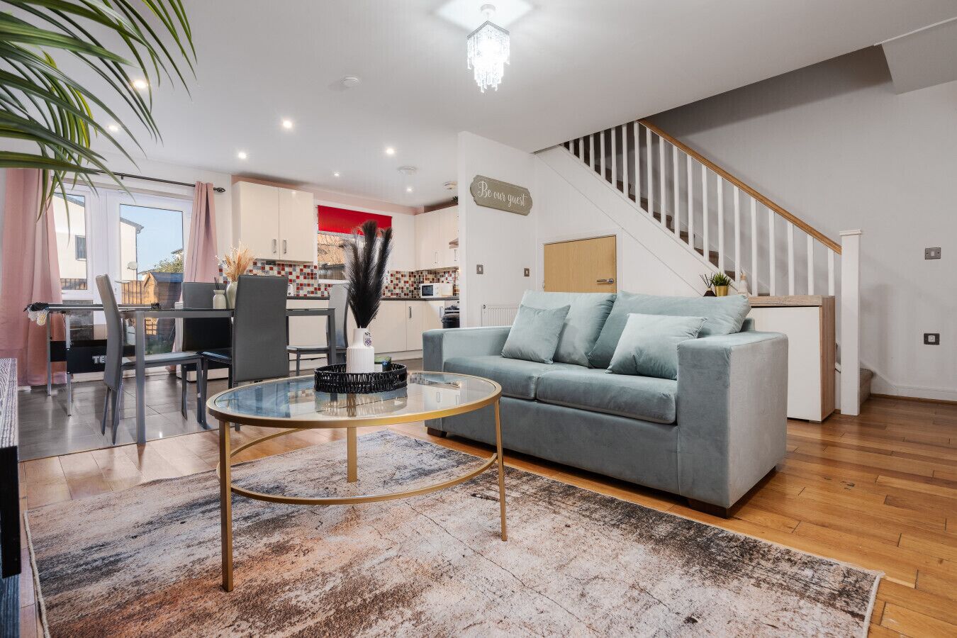Una sala de estar moderna con un sofá gris, una mesa de centro de vidrio y una escalera que sube a un nivel superior.