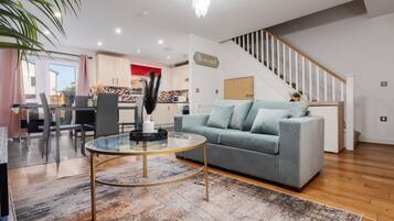 Una sala de estar moderna con un sofá gris, una mesa de centro de vidrio y una escalera que sube a un nivel superior.