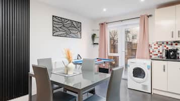 A modern kitchen with a washing machine, a dining area with a glass table, and a pool table.