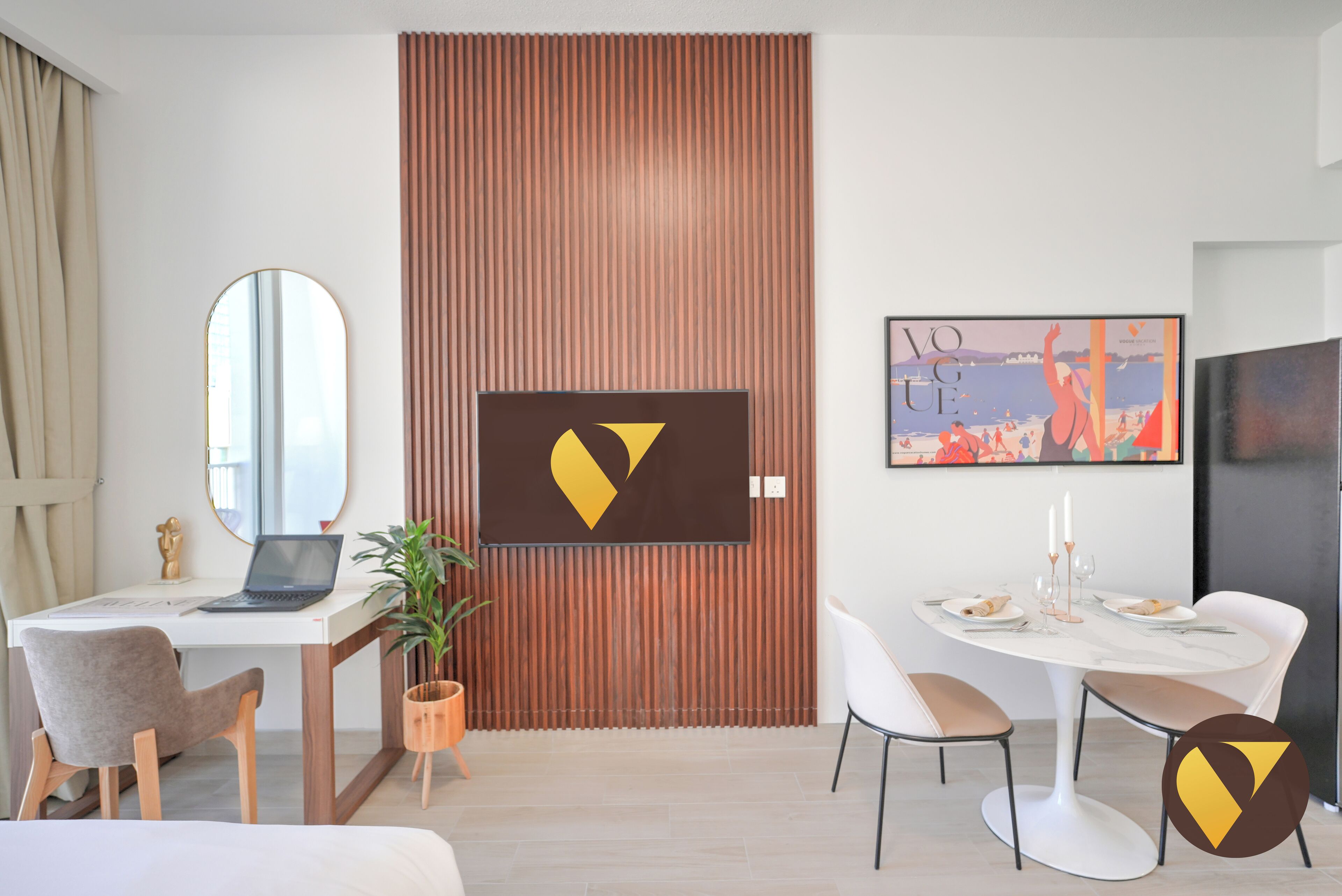 A modern hotel room with a wooden partition, a desk with a laptop, a dining table set for two, and a large mirror.