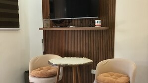 A modern living room with a flat-screen TV mounted on a wooden panel wall, two cushioned chairs with wooden legs, and a small round table. - Perfect getaway beach resort with a great view of Subic bay  (Olongapo)