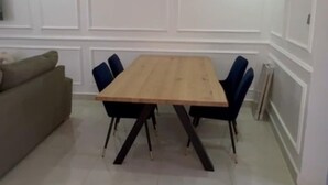 A dining area with a wooden table, blue chairs, a chandelier, and white paneled walls. - Apartment Building in Salagi (Salagi)