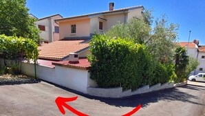 Une maison à deux étages, avec un toit recouvert de tuiles rouges, entourée de verdure et dotée d’une allée pavée.