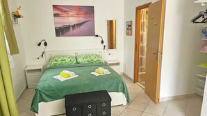 Une chambre à coucher bien rangée, avec un lit, des oreillers verts, une table de chevet, un tableau accroché au mur, une porte et un petit banc.