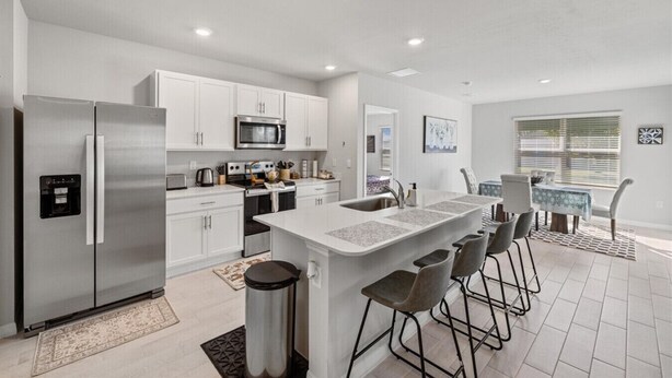 A modern kitchen with stainless steel appliances, white cabinetry, and a central island with bar stools.