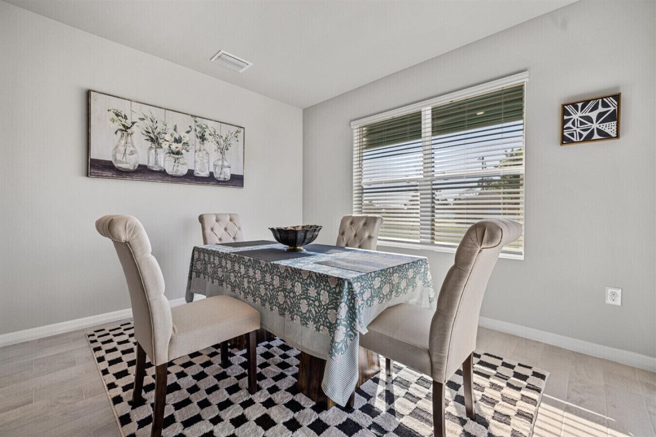 Un coin repas avec une table dressée pour quatre personnes, une nappe à motifs et un tapis à carreaux.