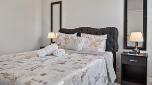 A neatly made bed with patterned bedding, two bedside lamps, a nightstand, and a large mirror on the wall.