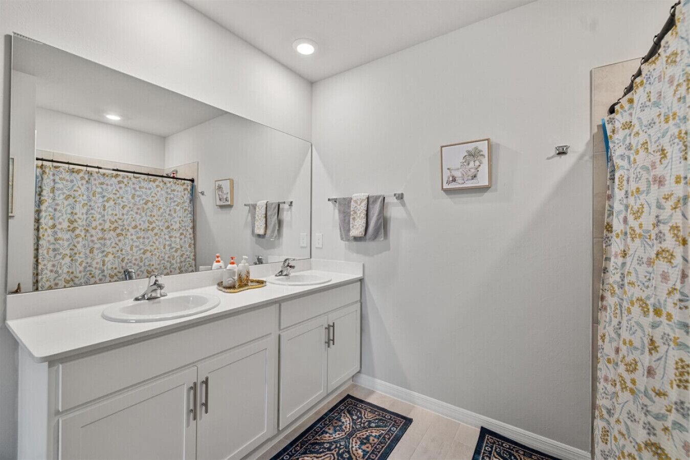 A bathroom with two sinks, a large mirror, and a shower curtain with a floral pattern.
