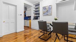 A modern kitchen with white cabinetry and a blue countertop. There are two chairs at a table with a vase of flowers.