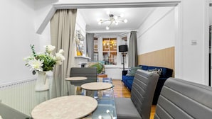 A modern living room with a glass coffee table, grey sofa, and a dining area with a glass table.
