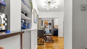 A modern kitchen with white cabinets, a wooden countertop, and a built-in oven. There is a dining area with a blue sofa and a coffee table.
