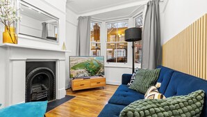 A living room with a fireplace, a large TV, a blue sofa, and a view of a cityscape through large windows.