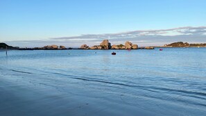 Une plage paisible avec une eau claire, de gros rochers et quelques bateaux.