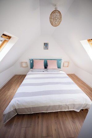 A bedroom with a sloped ceiling, a bed with striped bedding, a teal headboard, and a hanging light fixture.