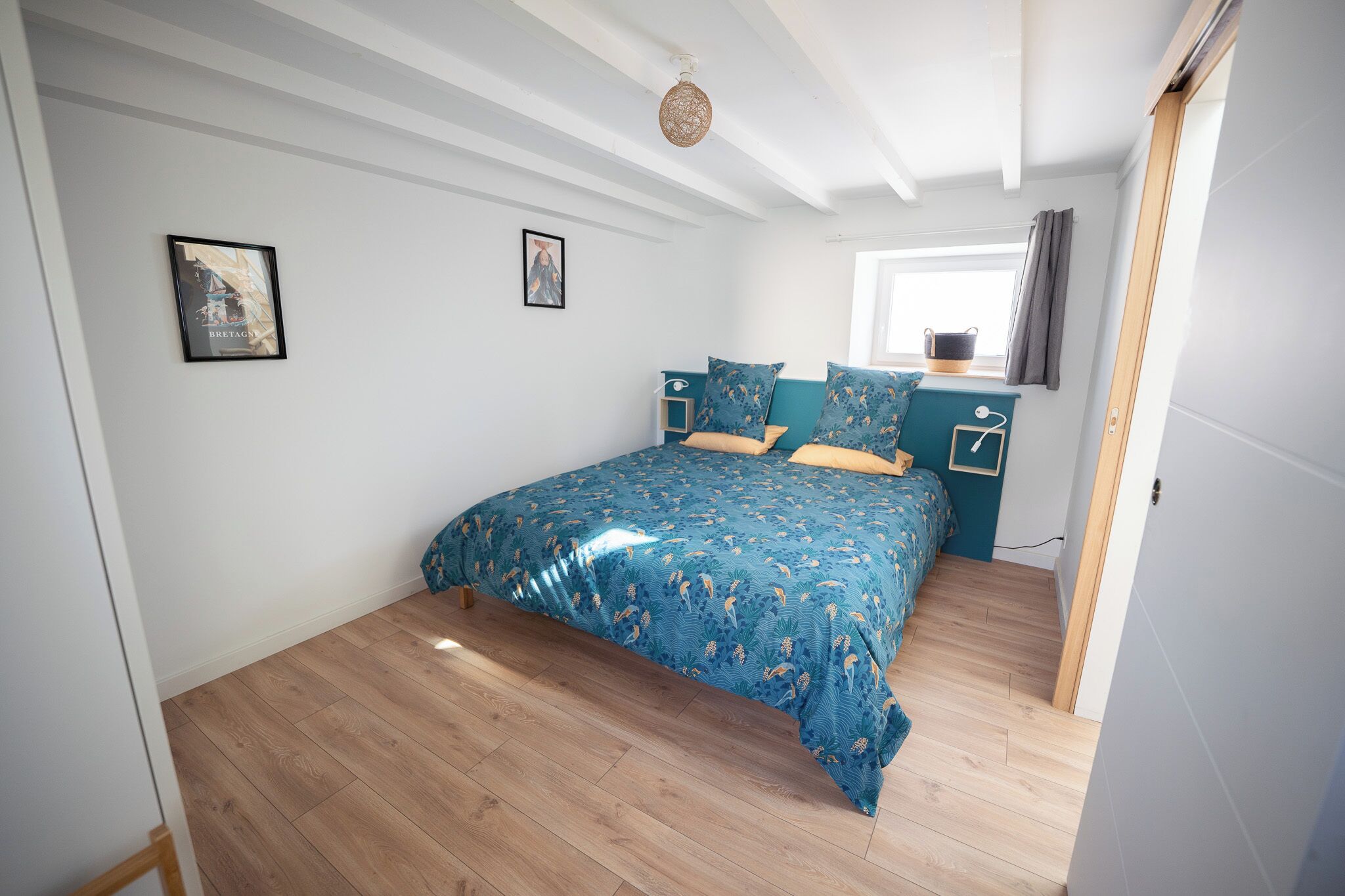 Un dormitorio con cama, mesita de noche, ventana con cortinas y puerta.