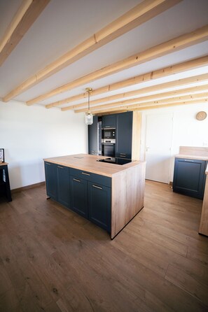 Een keuken met houten balken, een centraal eiland, donkere kastjes en een magnetron.