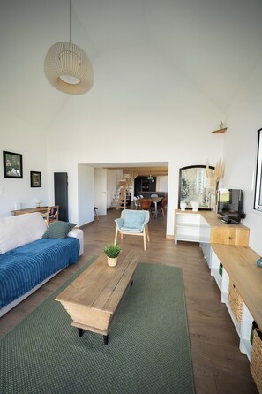 A modern living room with a sofa, a coffee table, and a TV. There is a staircase leading to another level.