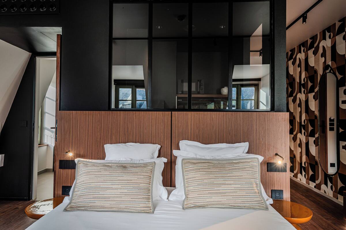A modern hotel room with a large bed, wooden headboard, and a large mirror above the bed.