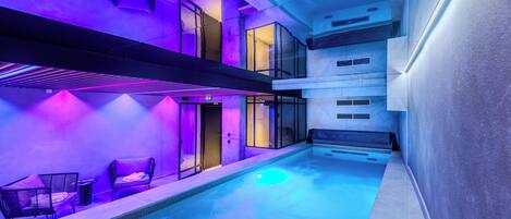 A modern indoor pool area with seating and a ceiling light.