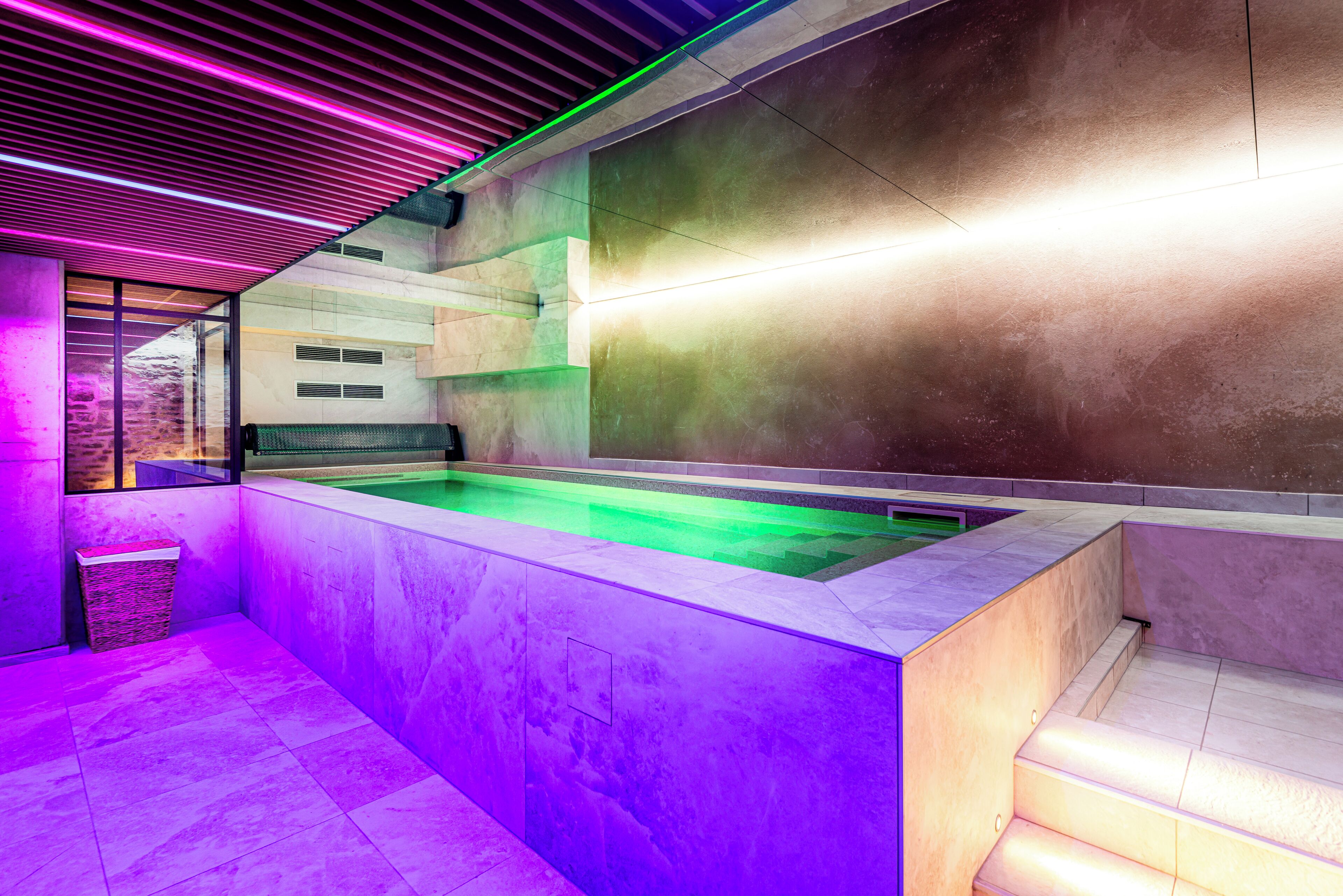 Un moderno espacio de spa con una amplia piscina climatizada, una pared de piedra y un techo de madera con iluminación de neón.