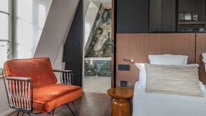 A modern hotel room with a bed, a chair, and a view of a balcony. - Appartements d'Anne - Saint Malo (Saint-Malo)