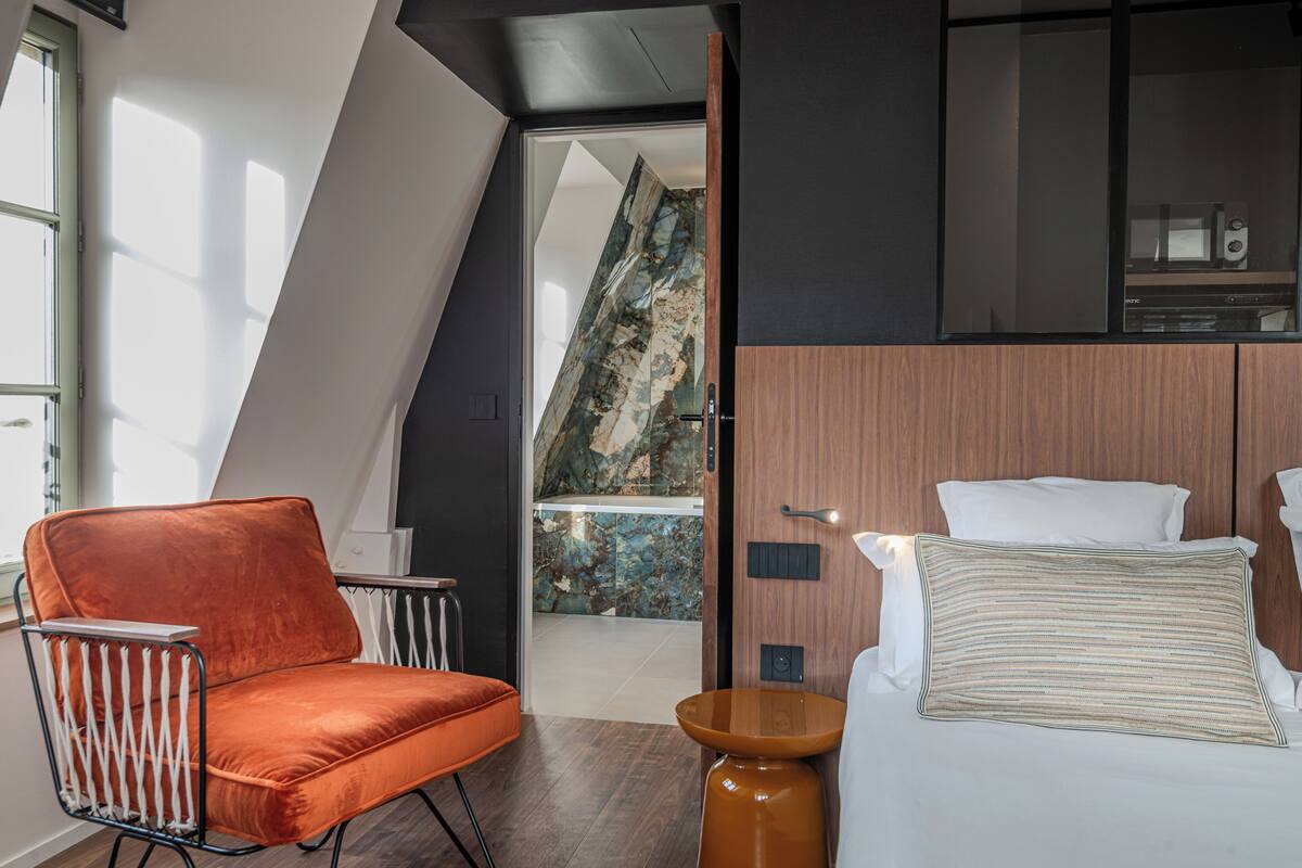 A modern hotel room with a bed, a chair, and a view of a balcony.