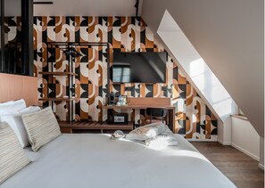 Una habitación de hotel moderna con una cama grande, un escritorio y un televisor de pantalla plana, y una pared con un diseño decorativo.