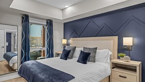 Een moderne slaapkamer met een groot bed, twee nachtkastjes, een raam met gordijnen en uitzicht op de omgeving.