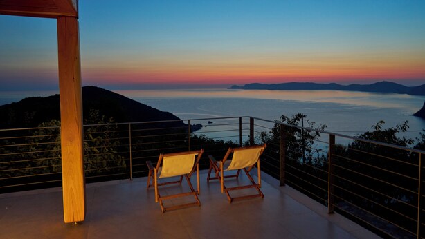 Un balcón con dos sillas de madera y vista al mar al atardecer.