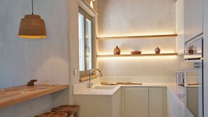 Cocina compacta con barra de madera, taburetes, pileta y estantes empotrados con objetos decorativos.