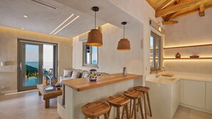 Una cocina moderna con una isla central, taburetes de madera, lámparas colgantes y vista al océano a través de amplios ventanales.