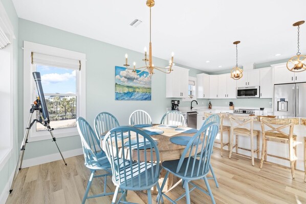 Une cuisine moderne avec des meubles blancs, un coin repas avec des chaises bleues et un télescope sur un trépied près de la fenêtre.