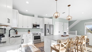 A modern kitchen with white cabinetry, stainless steel appliances, and a central island with wooden chairs. - Pool | Gulf Views | Outdoor Shower (Port St. Joe)