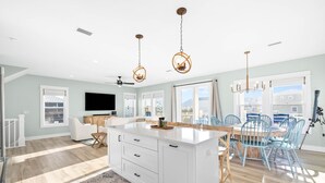 A spacious kitchen with a large island, a dining area with blue chairs, and a TV mounted on the wall. - Pool | Gulf Views | Outdoor Shower (Port St. Joe)