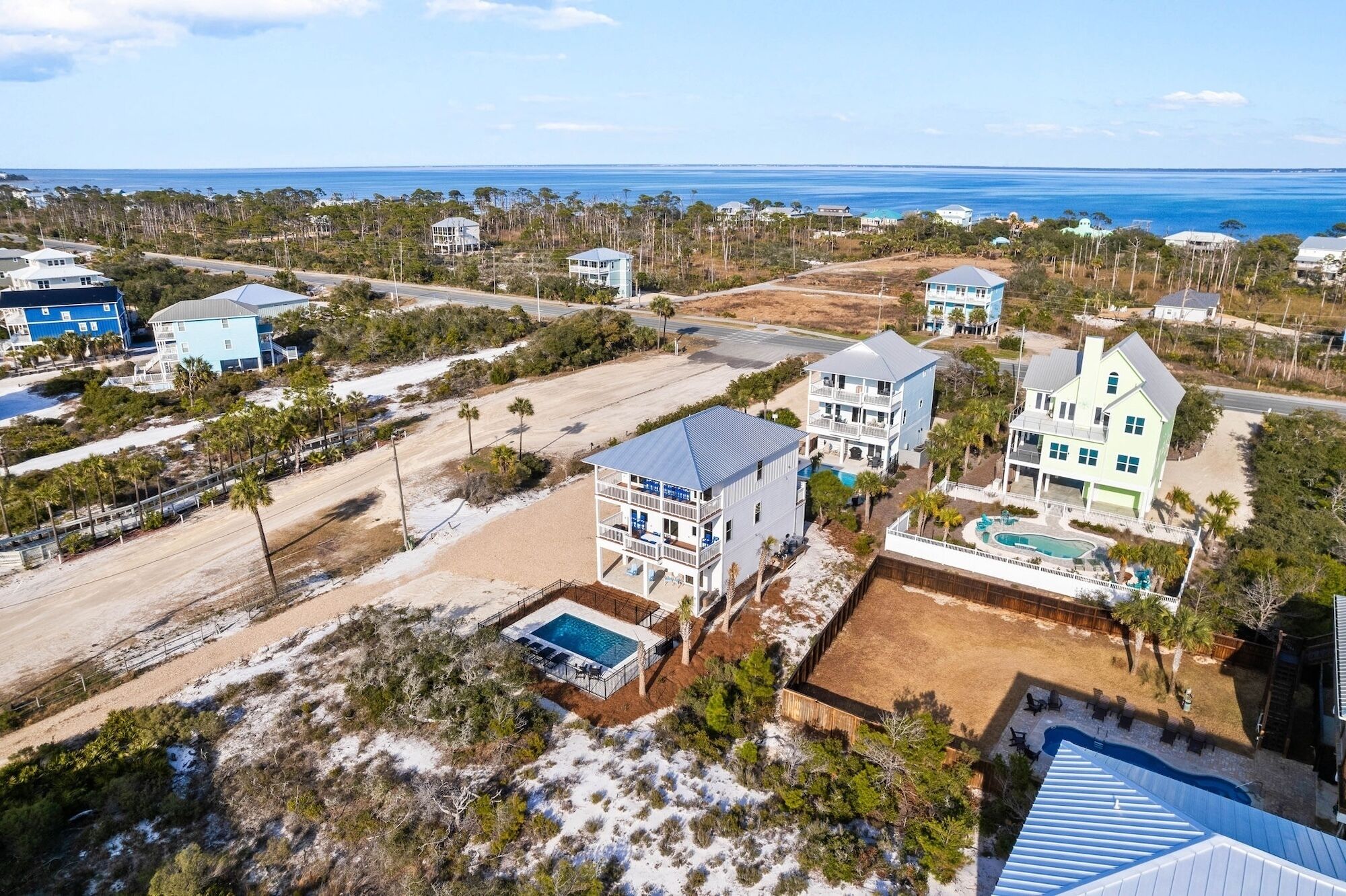 Vista aerea di una zona residenziale costiera con diverse case, una piscina e una spiaggia.