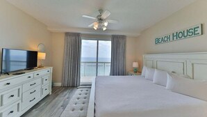 Habitación de hotel con cama, televisor, ventilador de techo y vista al mar.