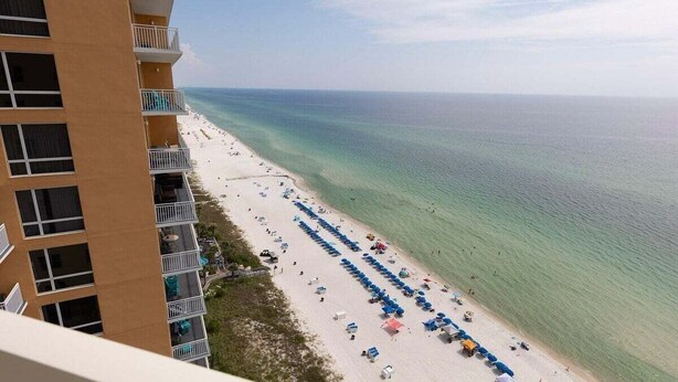 Un hotel moderno de gran altura con balcones que dan a una playa con hileras de sombrillas y tumbonas.