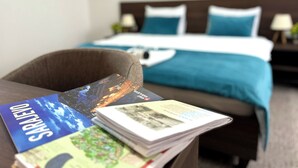 Una camera d'albergo con un letto, una scrivania con depliant e una sedia.